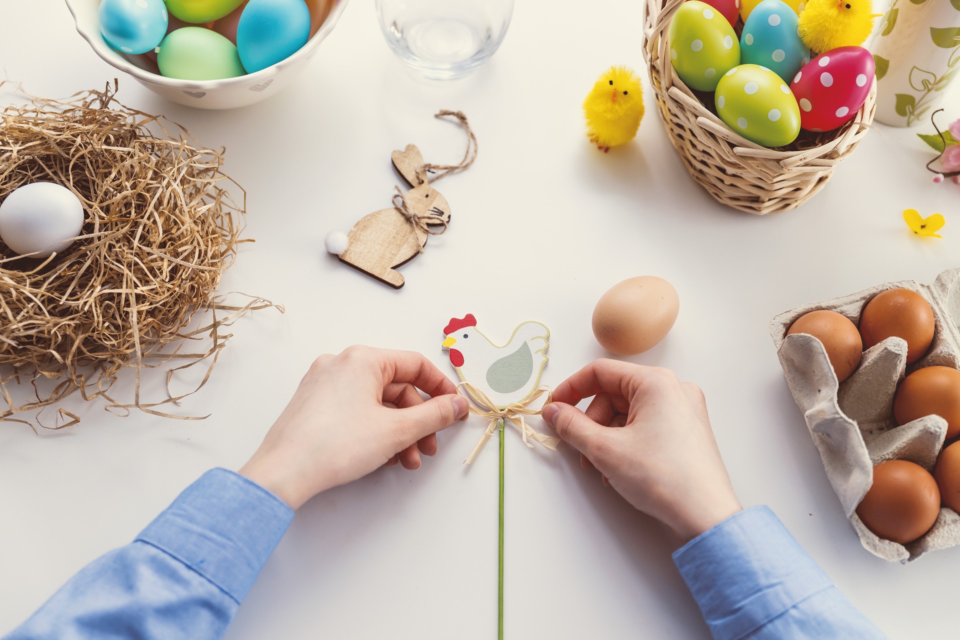 Two hands creating an Easter decoration on a table full of Easter eggs.