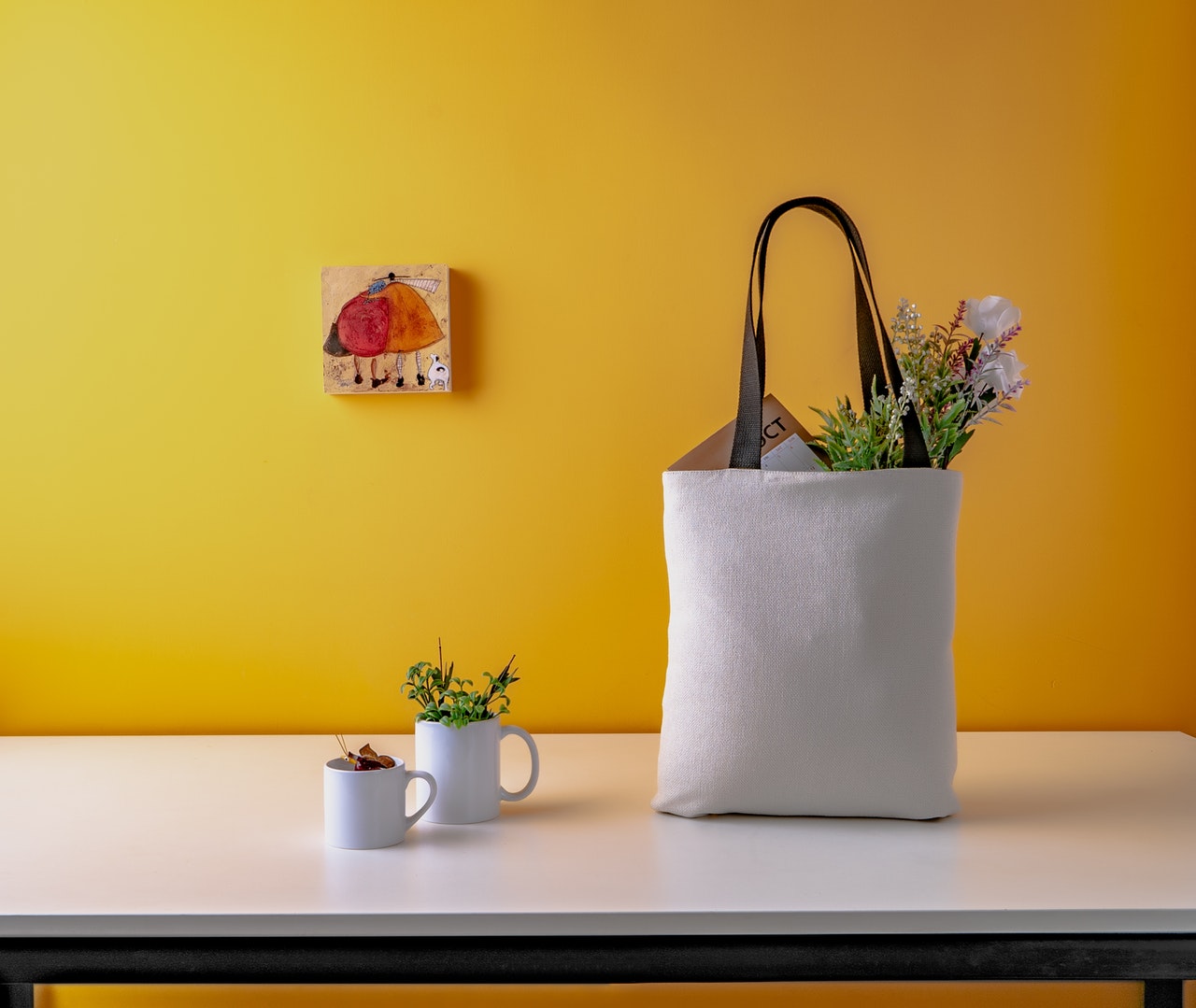 A yellow wall with a white table in front, two mugs, and a bag, representing ways to spruce up your living room for spring